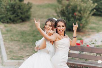 Wedding photo in nature. A brunette bride in a white long dress and her friend in a nude dress are...