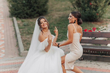 Wedding photo in nature. A brunette bride in a white long dress and her friend in a nude dress are...