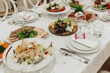 buffet table at a wedding. Cheese plate. Assortment of canaps. Banquet service. food, snacks with cheese, ham, prosciutto and fruit. Caesar salad. Glass glasses. Silver table sets.
