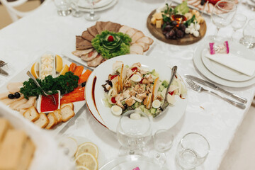 buffet table at a wedding. Cheese plate. Assortment of canaps. Banquet service. food, snacks with cheese, ham, prosciutto and fruit. Caesar salad. Glass glasses. Silver table sets.