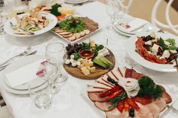 buffet table at a wedding. Cheese plate. Assortment of canaps. Banquet service. food, snacks with cheese, ham, prosciutto and fruit. Caesar salad. Glass glasses. Silver table sets.