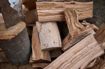 Still life with a heap of wood for making fire. Partial view of an ax or hatchet in a stump near firewood in rustic background. Renewable energy. Preparation for cold winter. Close-up. Nature