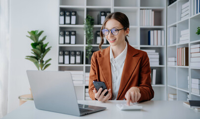 Confident business expert attractive smiling young woman typing laptop ang holding digital tablet on desk in creative office..