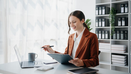 Confident business expert attractive smiling young woman typing laptop ang holding digital tablet on desk in creative office..