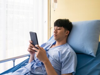 Asian young patient boy use smartphone for contact insurance and claim admit by himself in the bedroom at hospital