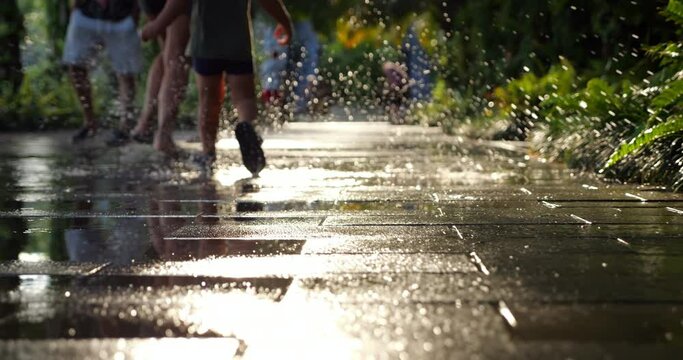 Happy little boy running over puddles with mom, low camera position and soft focus. Bright glowing water splash and drops, slow motion shot. Beauty of simple moments of life