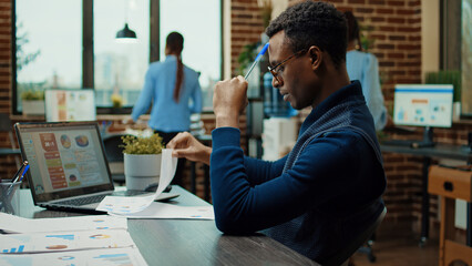 African american man brainstorming ideas to create new business vision, using papers and laptop with statistics to make perfect decision. Company analyst thinking about new research plan Generative AI - obrazy, fototapety, plakaty
