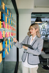 Secretary working in modern office in skyscraper, writing and sticking adhesive notes with tasks on...