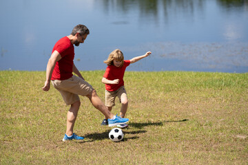 Obraz premium Dad and son playing football together on green meadow. Father and son having fun on football pitch. Dad with kid are having fun and playing football on grass outdoor. Friendly family. Fathers day.