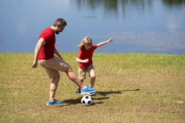 Dad and son playing football together on green meadow. Father and son having fun on football pitch. Dad with kid are having fun and playing football on grass outdoor. Friendly family. Fathers day.
