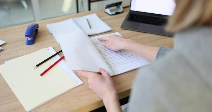Female person hands carefully open paper folder with script. Actress looks for own lines. Script lies on wooden office table with papers and stationery slow motion