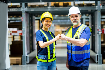 team of men and women wearing uniforms and helmets clenched their fists, confidently delivering professional cargo services successfully standing in the warehouse.