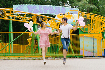Young couple in love runs with balloons and has fun in an amusement park