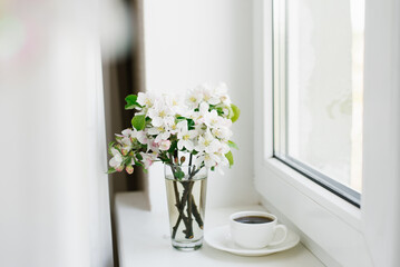 Cup of coffee on a white plate and a vase of flowers on the windowsill. Cozy Easter, spring still life.