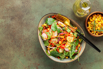 Fresh salad with vegetables. Arugula, spinach, cucumbers, tomato, onions carrots, corn andradishes in a plate on the table. Diet nutrition. Top view. Copy space
