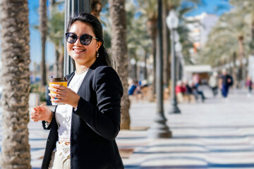 Obraz premium Smiling Asian Businesswoman in Professional Attire Enjoying a Takeaway Coffee
