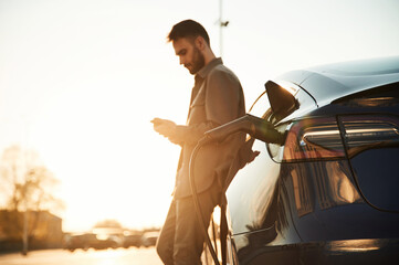 In the beautiful sunlight. Man is standing near his electric car outdoors