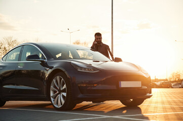Beautiful sunlight. Man is standing near his electric car outdoors