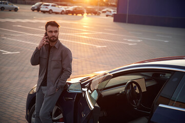 Fototapeta premium Evening time. Beautiful sunlight. Man is standing near his electric car outdoors