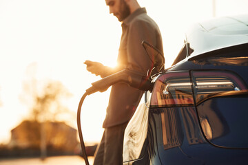 Beautiful sunlight. Man is standing near his electric car outdoors