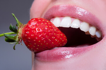 Strawberry in lips. Red strawberry in woman mouths close up. Closeup of smile with white healthy teeth.