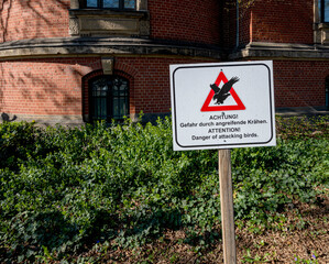 Obraz premium Hinweisschild vor einem Gebäude, Gefahr durch angreifende Krähen, Berlin, Deutschland