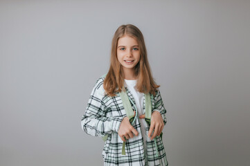 Obraz premium cheerful teenage girl 11,12,13 years old in a school uniform wears a backpack on a gray background. school fashion