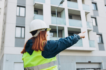Female engineer with white helmet pointing finger on a construction site, Architect on construction site check documents and business workflow near modern building.