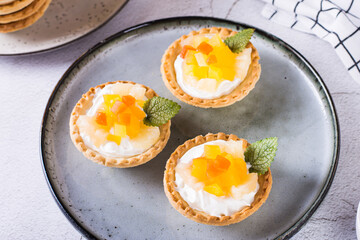 Appetizing tartlet dessert with whipped cream, canned fruit and mint on a plate