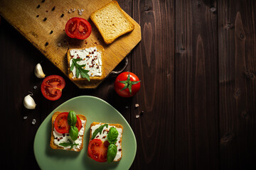 Delicious sandwiches of cream cheese with tomatos on a dark wooden background