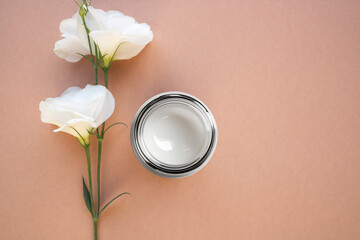 Obraz na płótnie Canvas A jar of moisturizing cream and a natural flower on a beige background. Top view, place for text.
