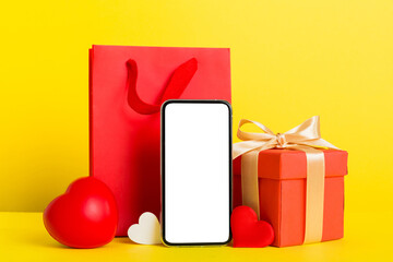 mobile phone with blank screen on colored background with hearts, calendar and gift box, valentine day concept perspertive view flat lay