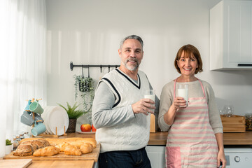 Caucasian senior mature couple drink a glass of milk in kitchen at home. 