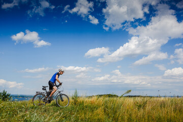 Obraz premium young athletic man on a bicycle riding the green meadow trail on sunny day