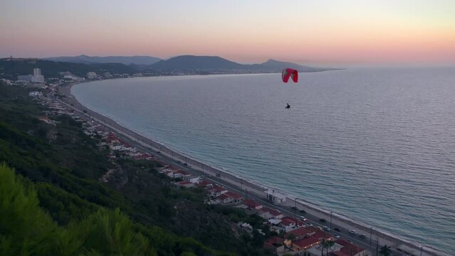 A man on a paraglider against the backdrop of the sea landscape and sunset sky.