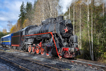 A steam locomotive with a retro train on a forest stretch. Russia