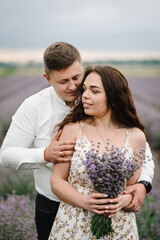 Family hugging in purple lavender field. Couple standing and enjoys floral glade, summer nature. France, Provence. Loving couple holding bouquet of lavender flowers at sunset. Honeymoon trip. Closeup.