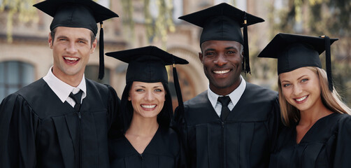 Group of happy graduates in mortarboards and formal wear looking at camera together
