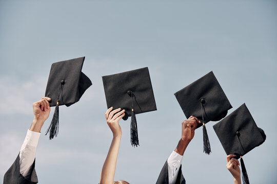 Close-up of many hands holding mortarboards against blue sky after graduation ceremony