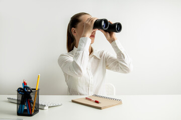 Young woman in a white shirt looks through binoculars while sitting at her workplace