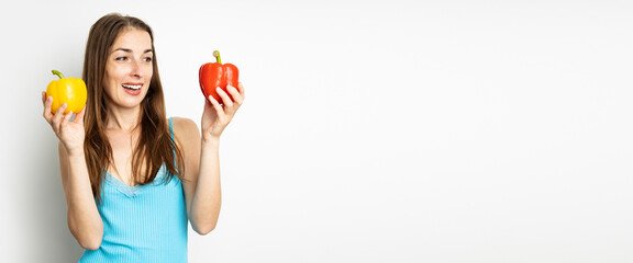 Smiling young woman holding fresh yellow and red paprika on white background. Banner