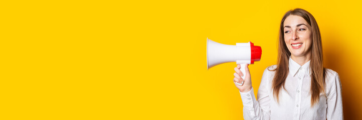 Friendly young woman holds a megaphone in her hands on a yellow background. Hiring concept, help...