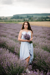 Fototapeta na wymiar Girl standing in lavender flowers field. A woman walk on the lavender field. Enjoy the floral glade, summer nature. Natural cosmetics concept. Female hold bouquet flowers and collect lavender. Closeup