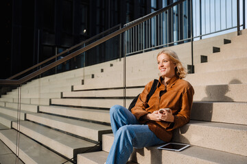 Smiling woman using smartphone while sitting on stairs outdoors