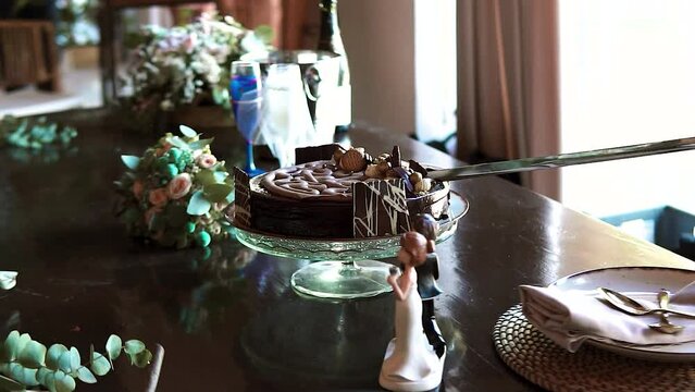 Chocolate cake being cut by a sword at a wedding. Flowers and wedding figures.