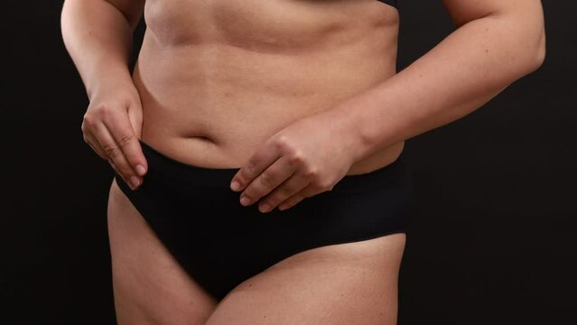 Unrecognizable fat woman wearing black seamless sportswear, adjusting trying on sports panties, showing stretch marks, caressing massaging skin of belly on black background. Weight loss, Generative AI