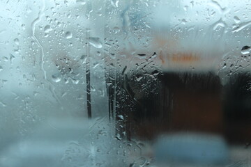 A close-up of the wet glass window of a motor vehicle, with raindrops and snow falling in the freezing indoor backgrounds.