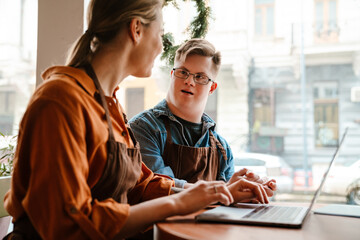 Woman using laptop while training man with down syndrome to work in cafe
