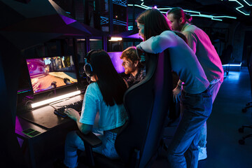 Group of people watching their friend playing video game and assisting her in cybersport club