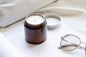 Soy wax aroma candle in brown jar on bed , with fashion glasses. Candle mockup design